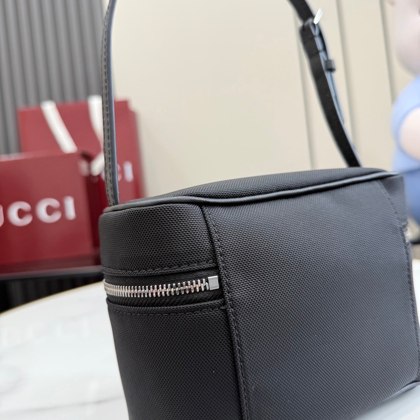 Black pebbled leather mini shoulder bag side view with top zipper and strap edge