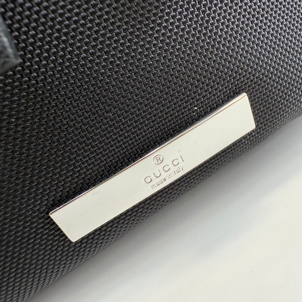 Gucci bag close-up with black textured fabric and silver Gucci logo plaque