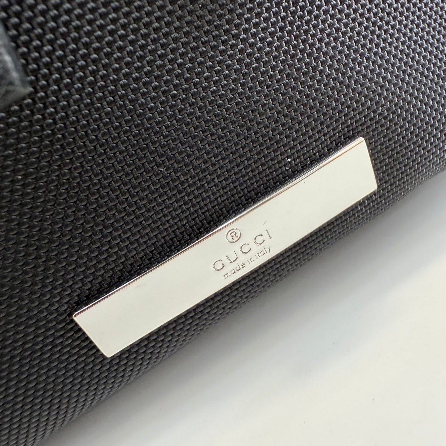 Gucci bag close-up with black textured fabric and silver Gucci logo plaque