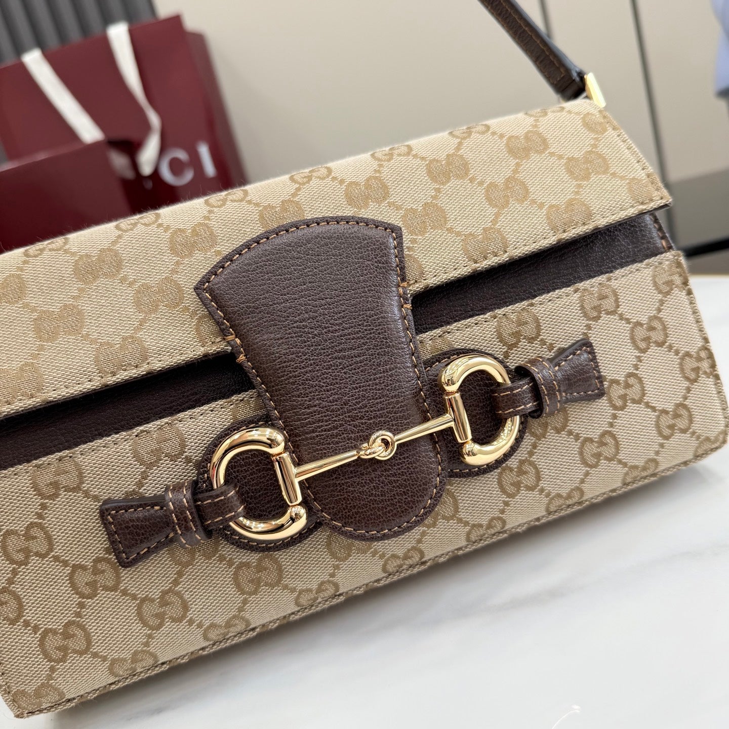 Gucci bag close-up of front closure, GG canvas with dark leather panel and gold hardware