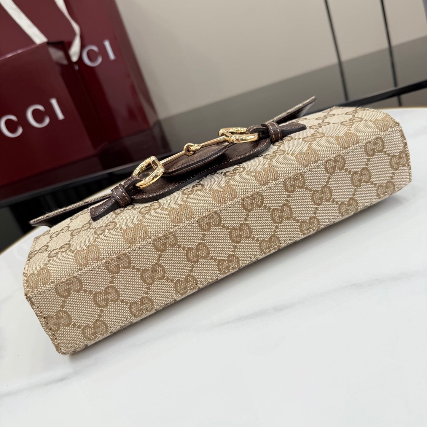 Gucci bag lying flat, GG canvas body with dark leather strap and gold-tone clasp