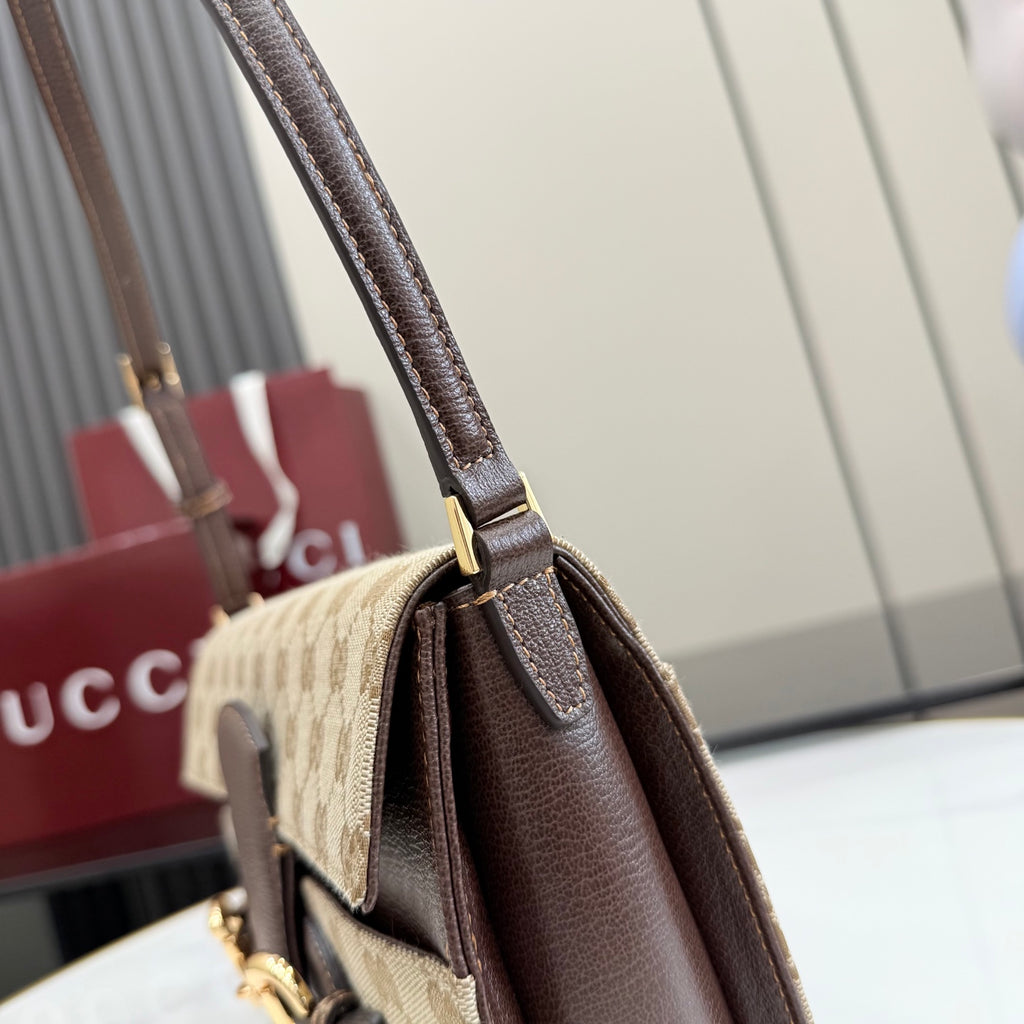 Designer bag close-up: brown leather top handle with gold clasp on beige canvas