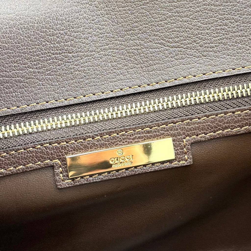 Gucci bag detail with gold logo plaque and zipper, dark leather exterior