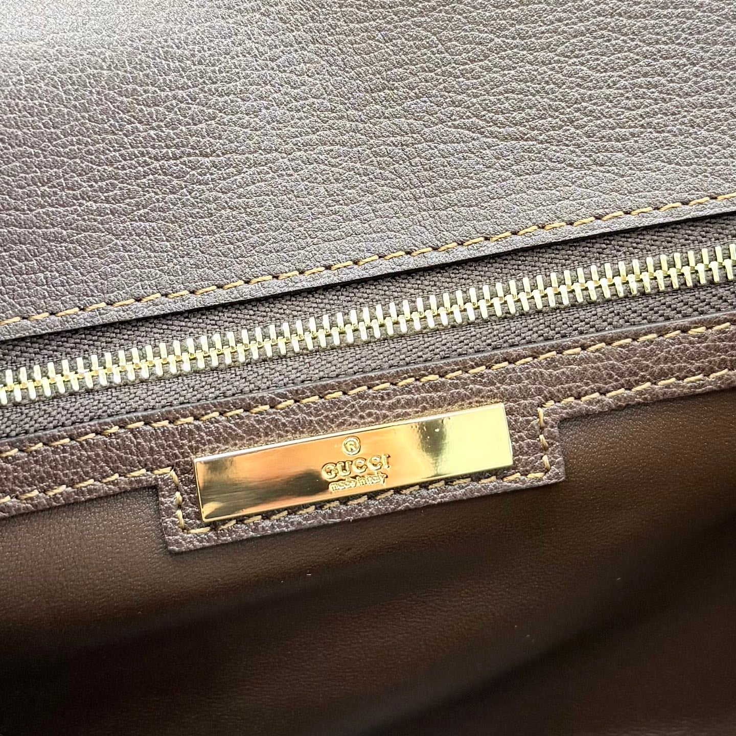 Gucci bag detail with gold logo plaque and zipper, dark leather exterior
