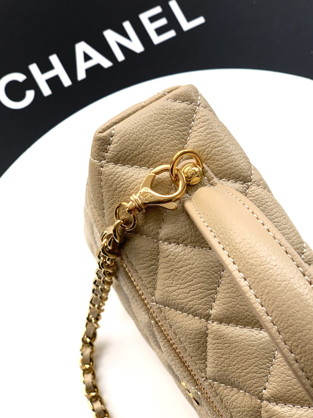 Beige quilted bag close-up with top clasp ring and gold zipper pull