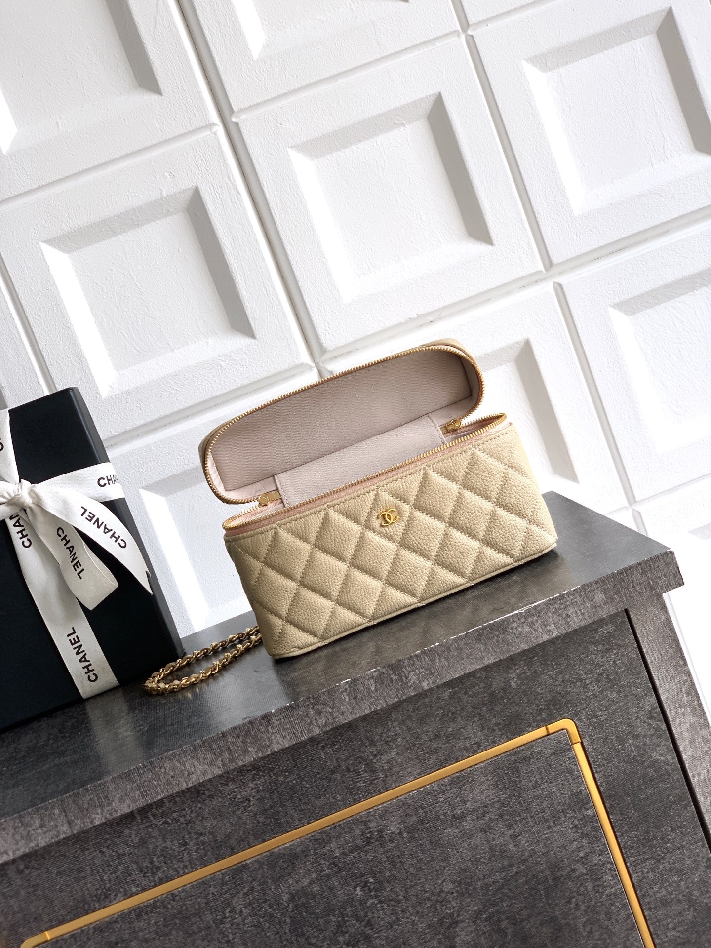 Light beige quilted handbag shown open with interior lining and gold zipper trim