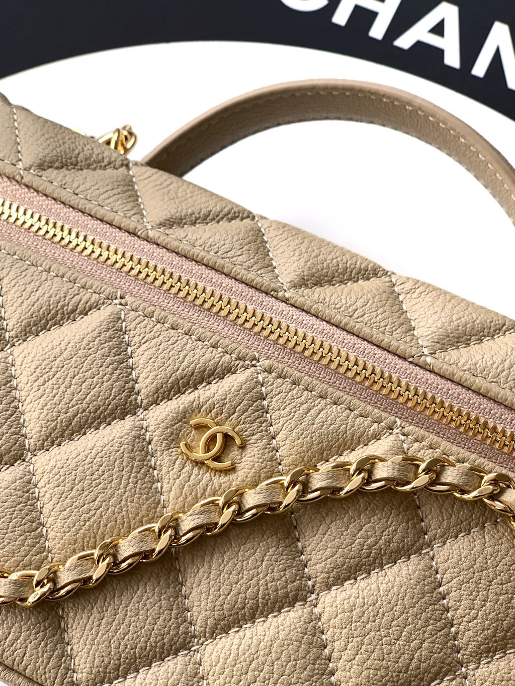 Quilted beige bag close-up with gold zipper and gold chain detail across the front