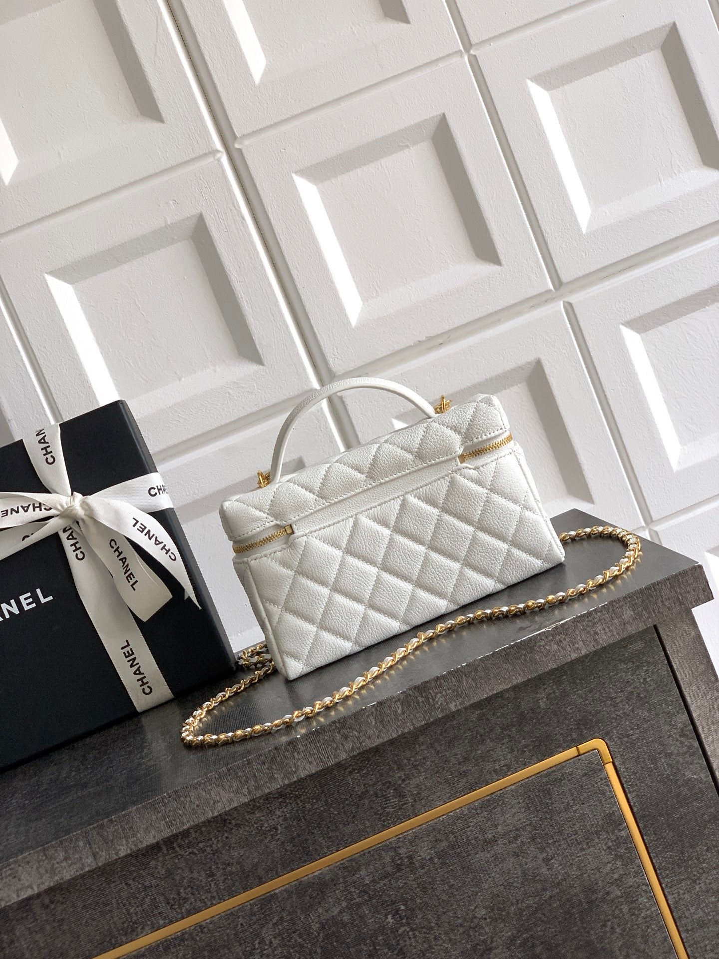 White quilted handbag with curved top handle and gold chain strap