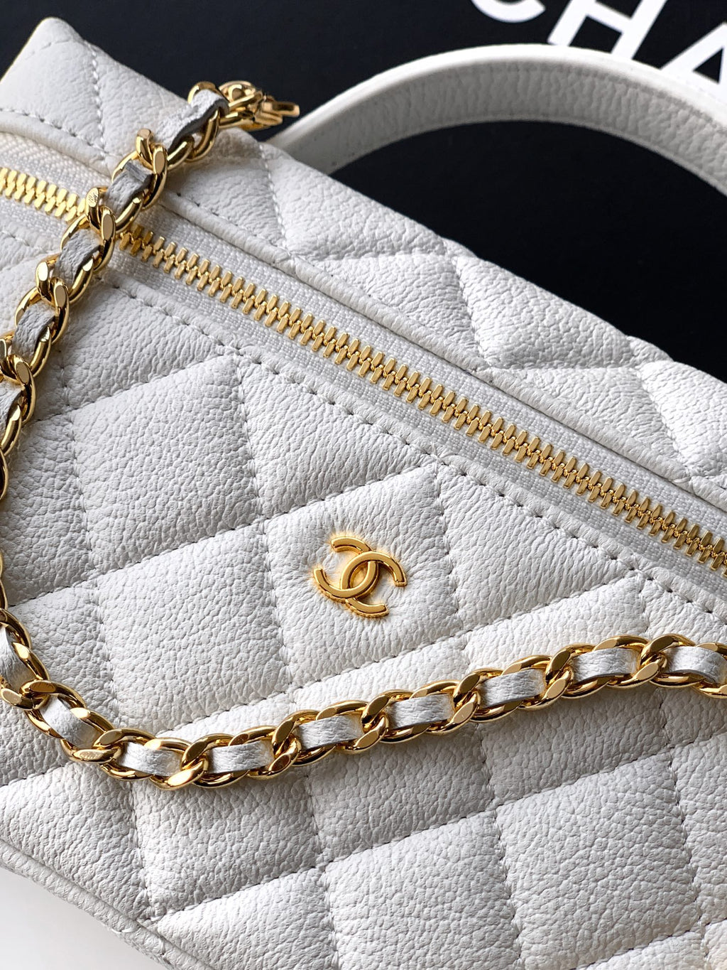 Close-up of white quilted bag with gold zipper and CC emblem