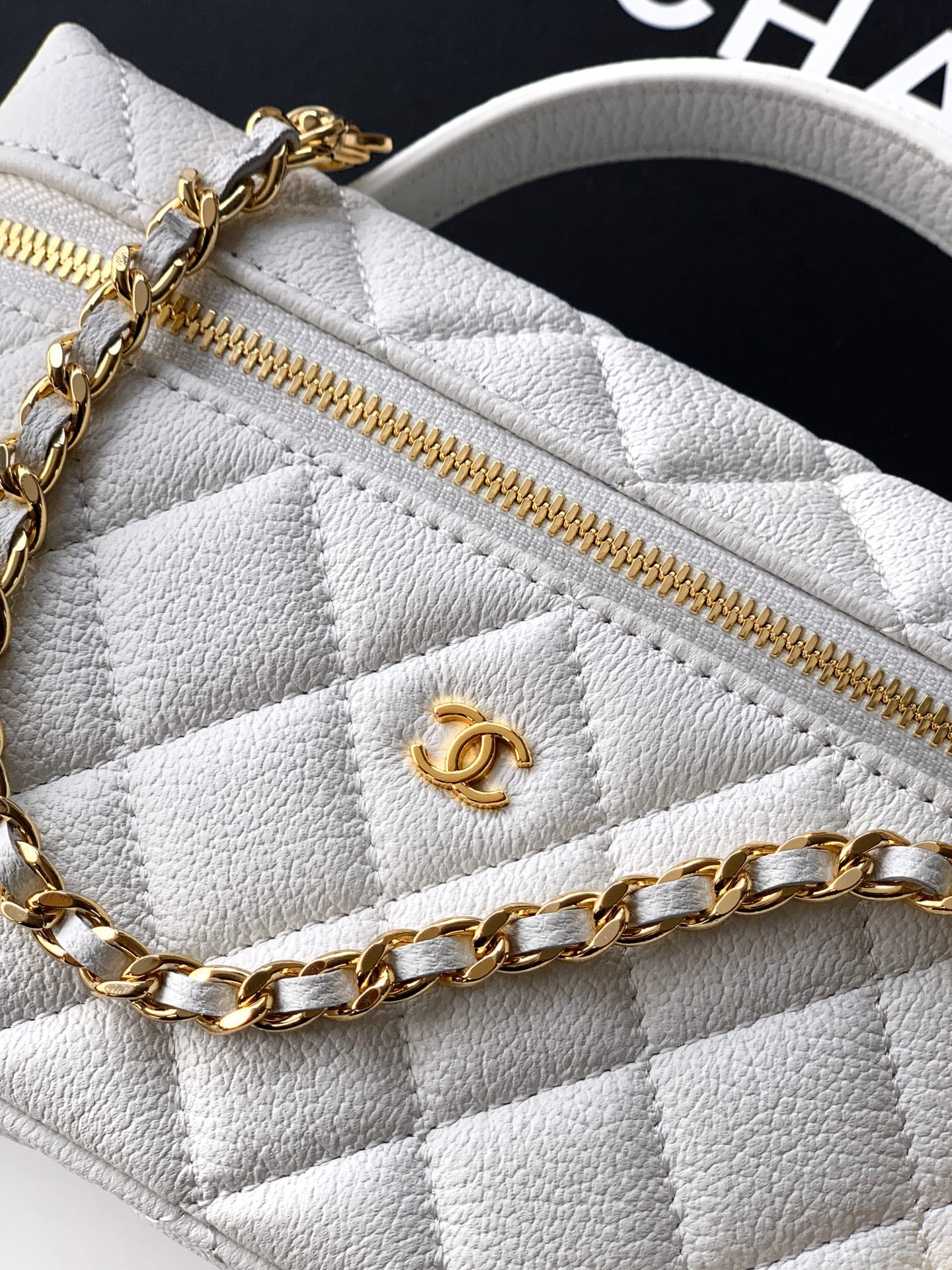 Close-up of white quilted bag with gold zipper and CC emblem