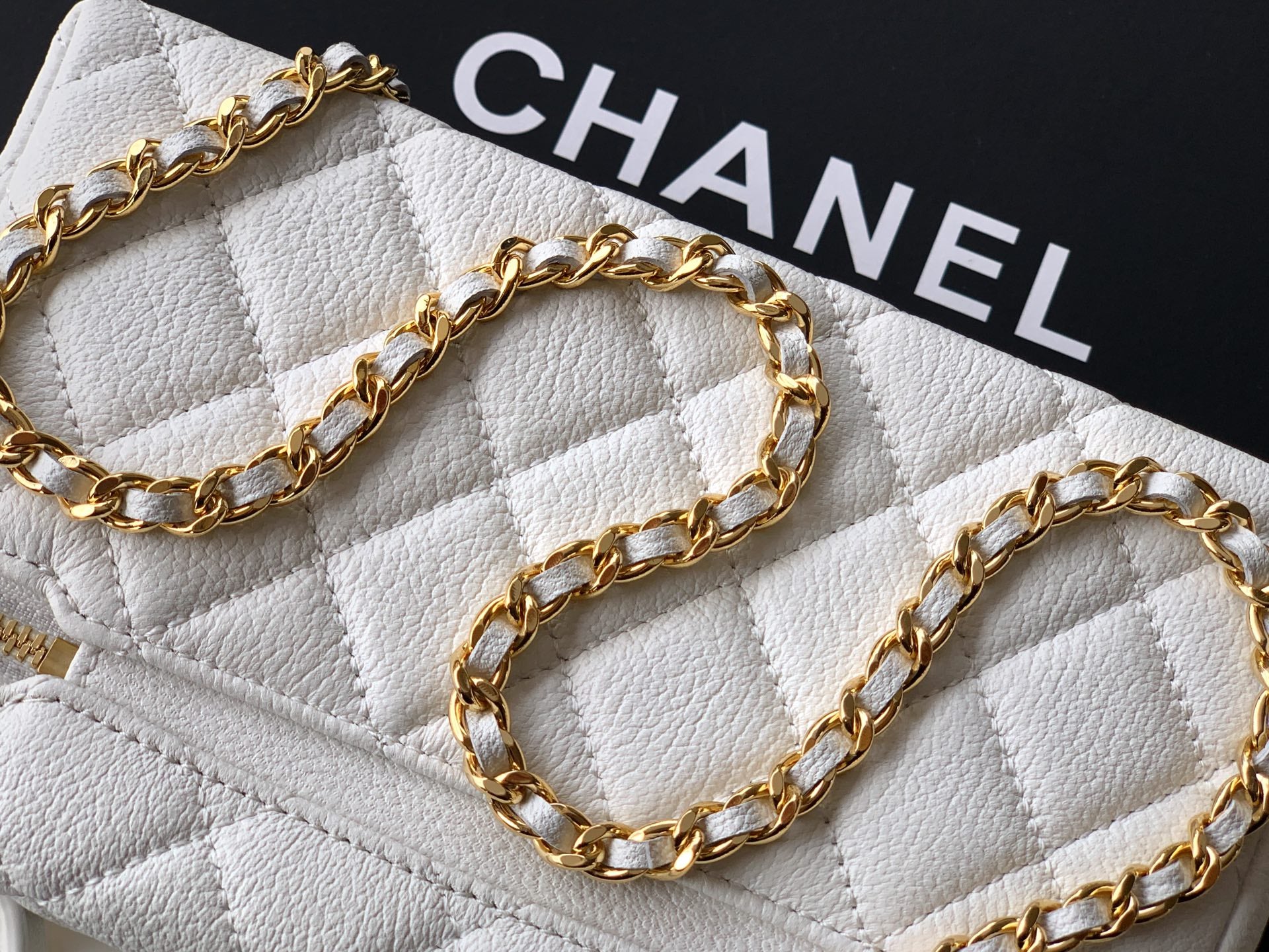 Close-up of gold chain strap on white quilted bag with CHANEL text