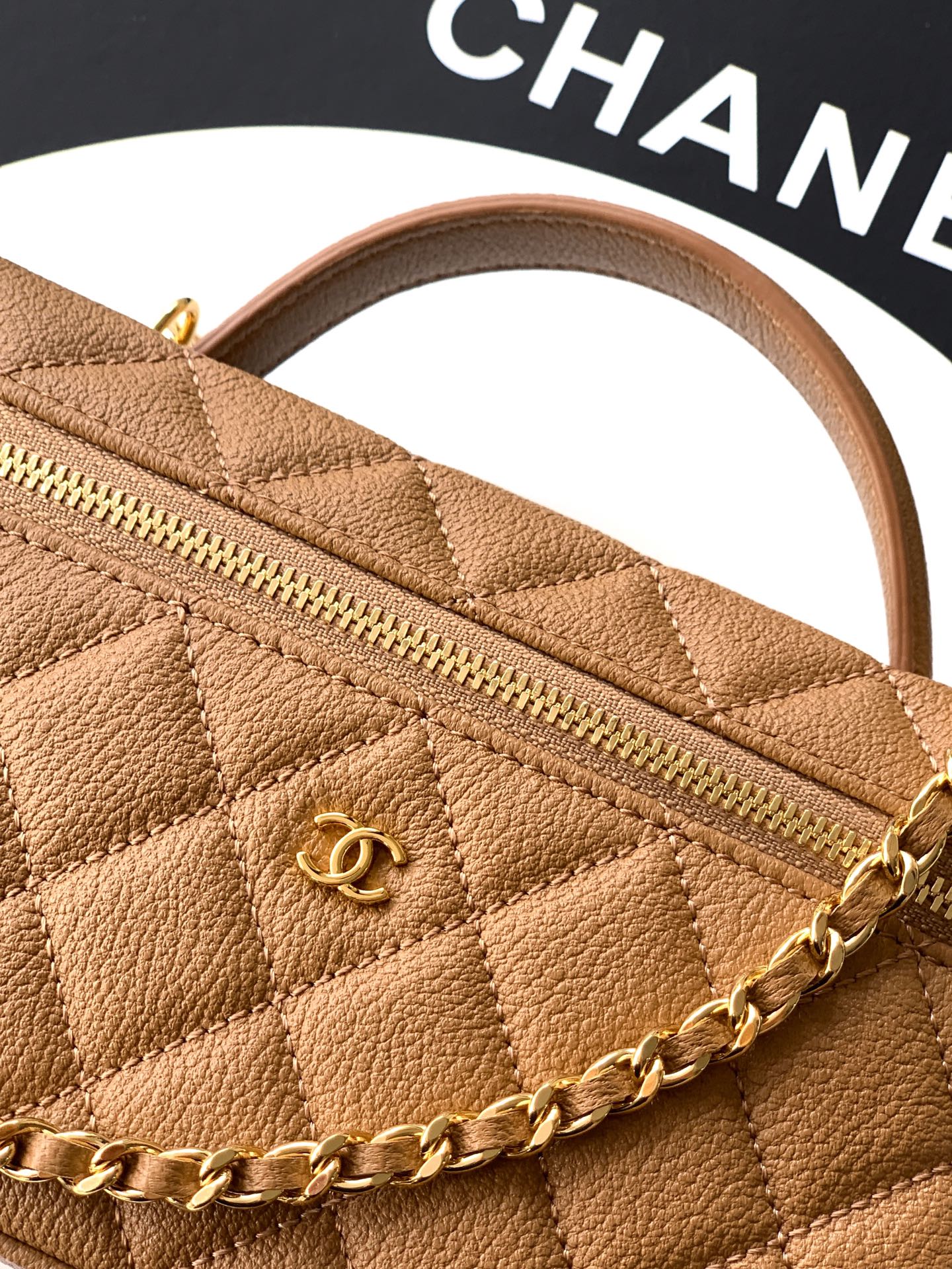 Tan quilted handbag close-up: gold zipper, chain strap, stitched diamond pattern.