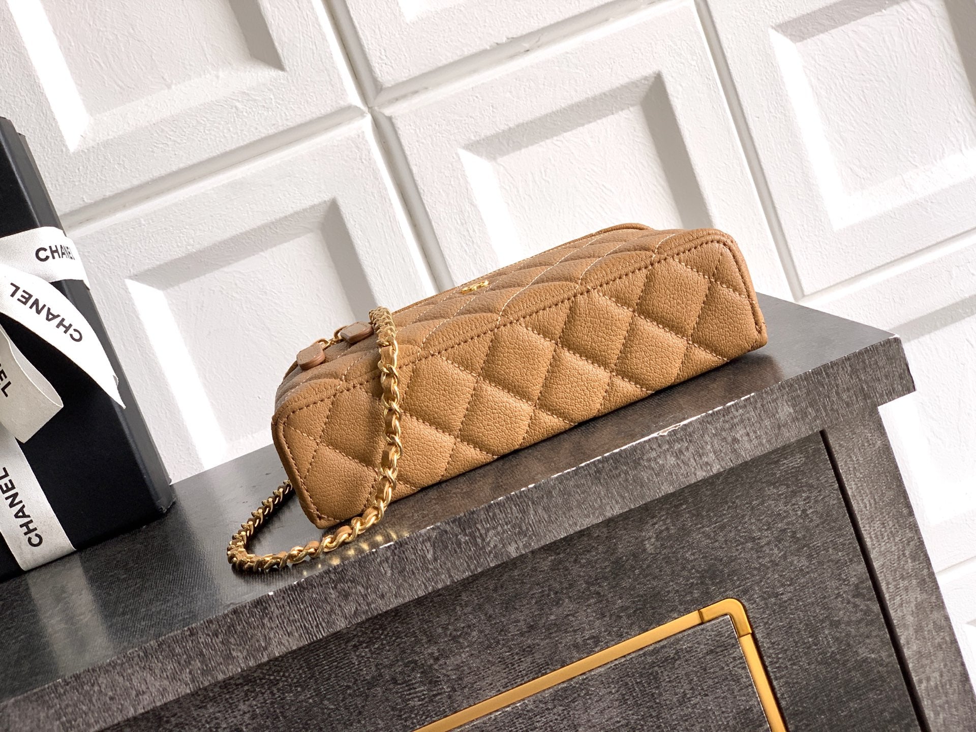 Tan quilted handbag with gold chain strap and zip top, stitched diamond pattern.