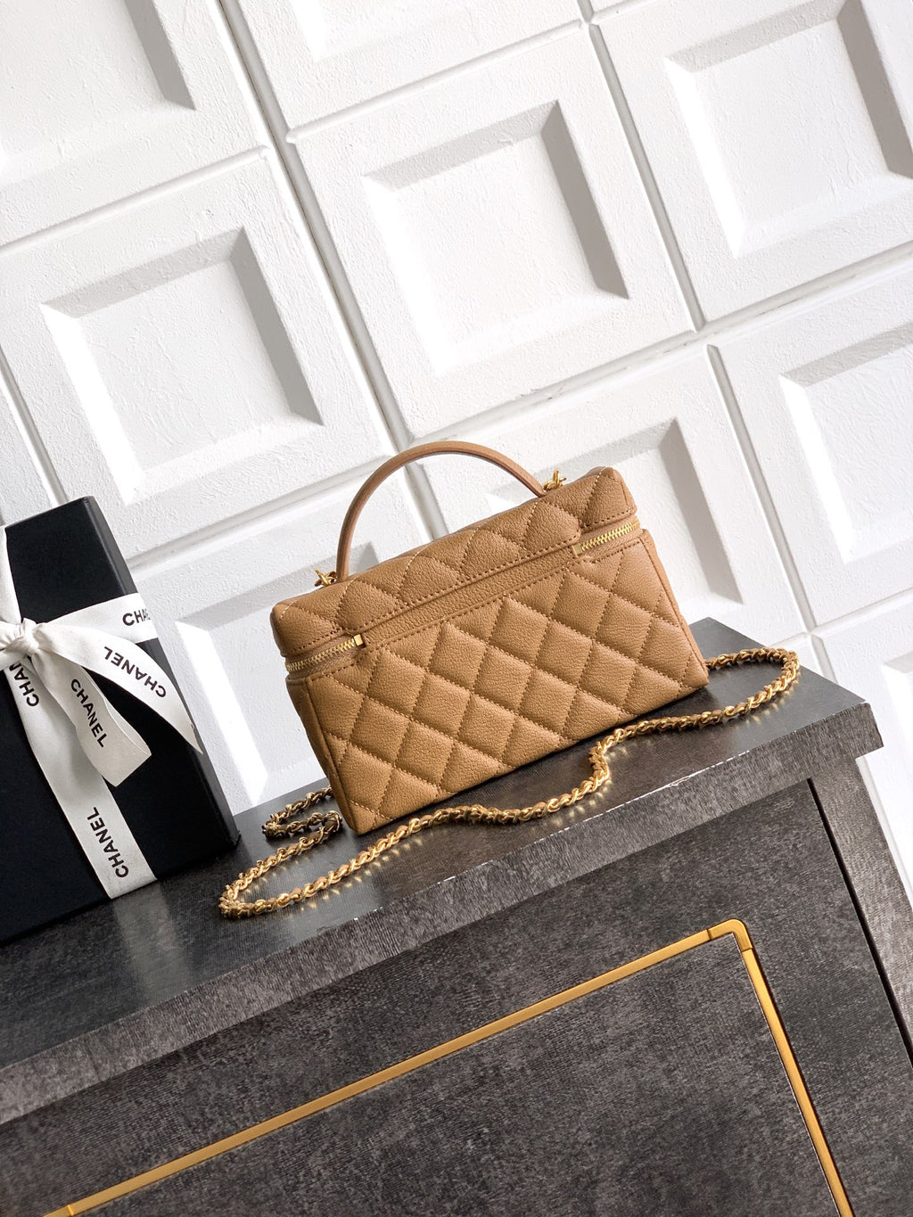 Tan quilted handbag with curved handle, gold chain strap, front pocket detail.