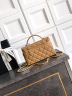 Tan quilted handbag with curved handle, gold chain strap, front pocket detail.