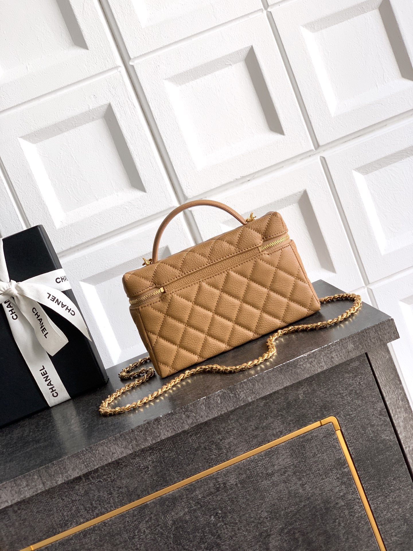 Tan quilted handbag with curved handle, gold chain strap, front pocket detail.
