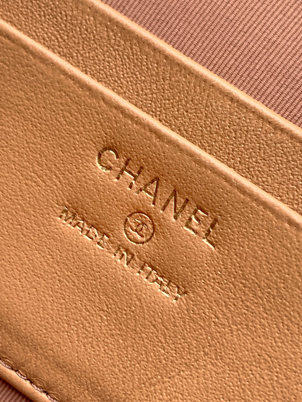 Tan quilted handbag close-up of embossed CHANEL logo on leather surface.