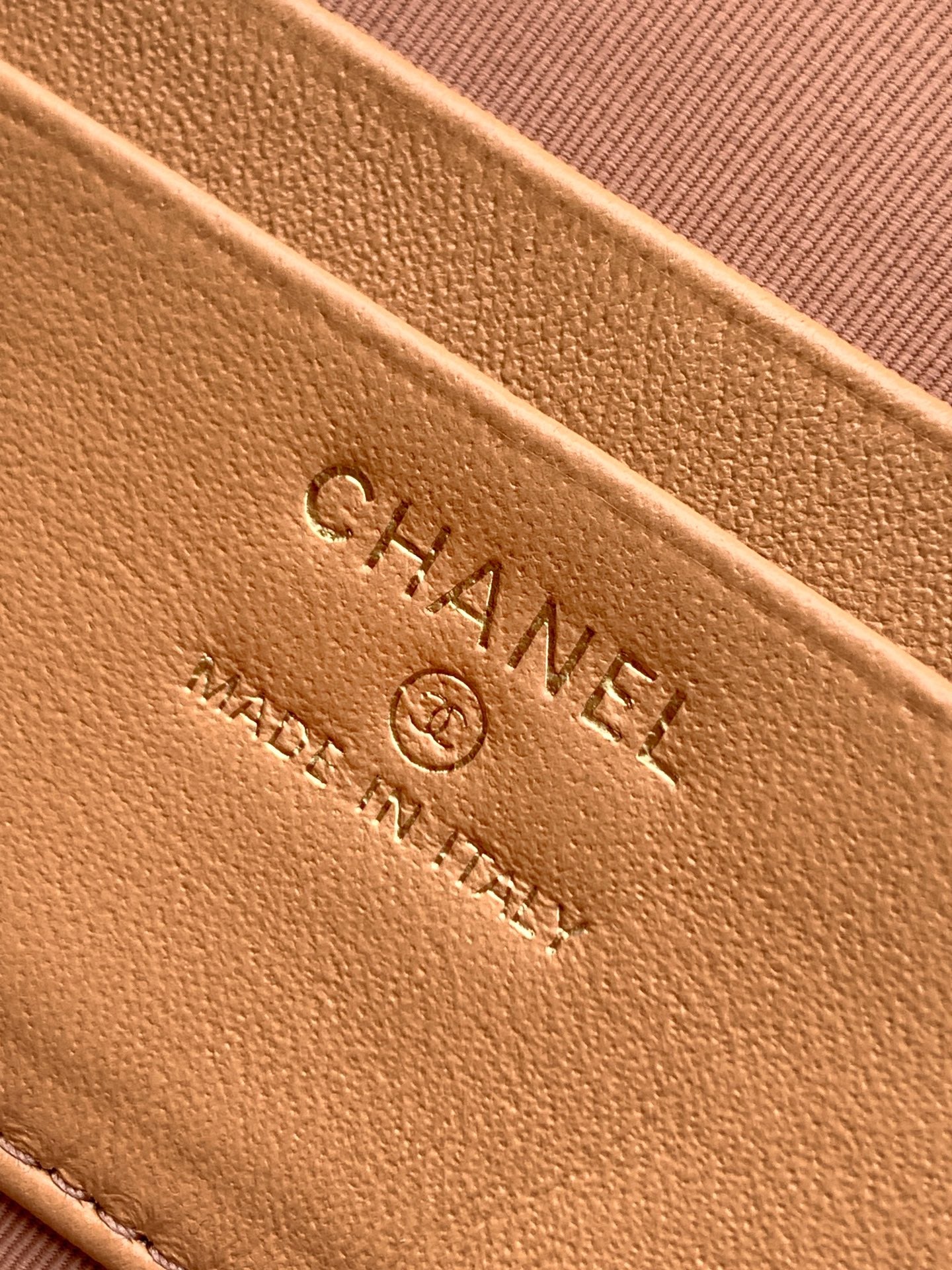 Tan quilted handbag close-up of embossed CHANEL logo on leather surface.