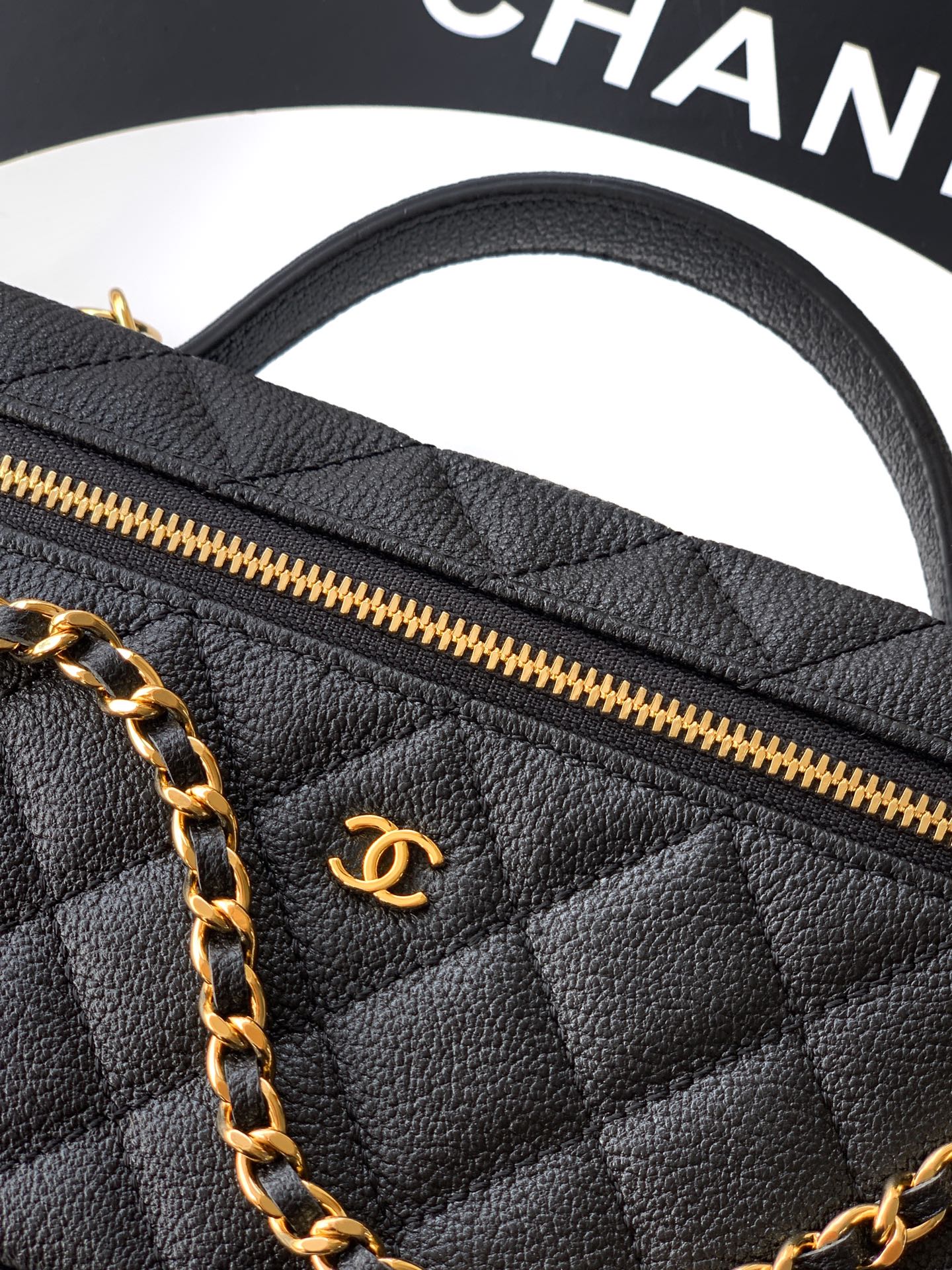 Black quilted handbag close-up showing gold zipper and gold Chanel emblem.