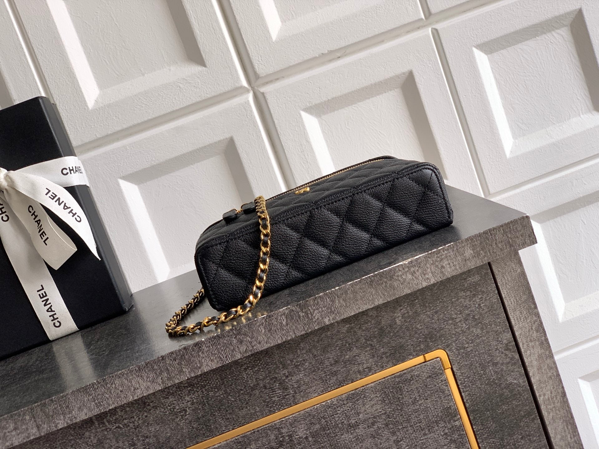 Black quilted mini handbag with gold chain strap and curved top handle, zip closure.
