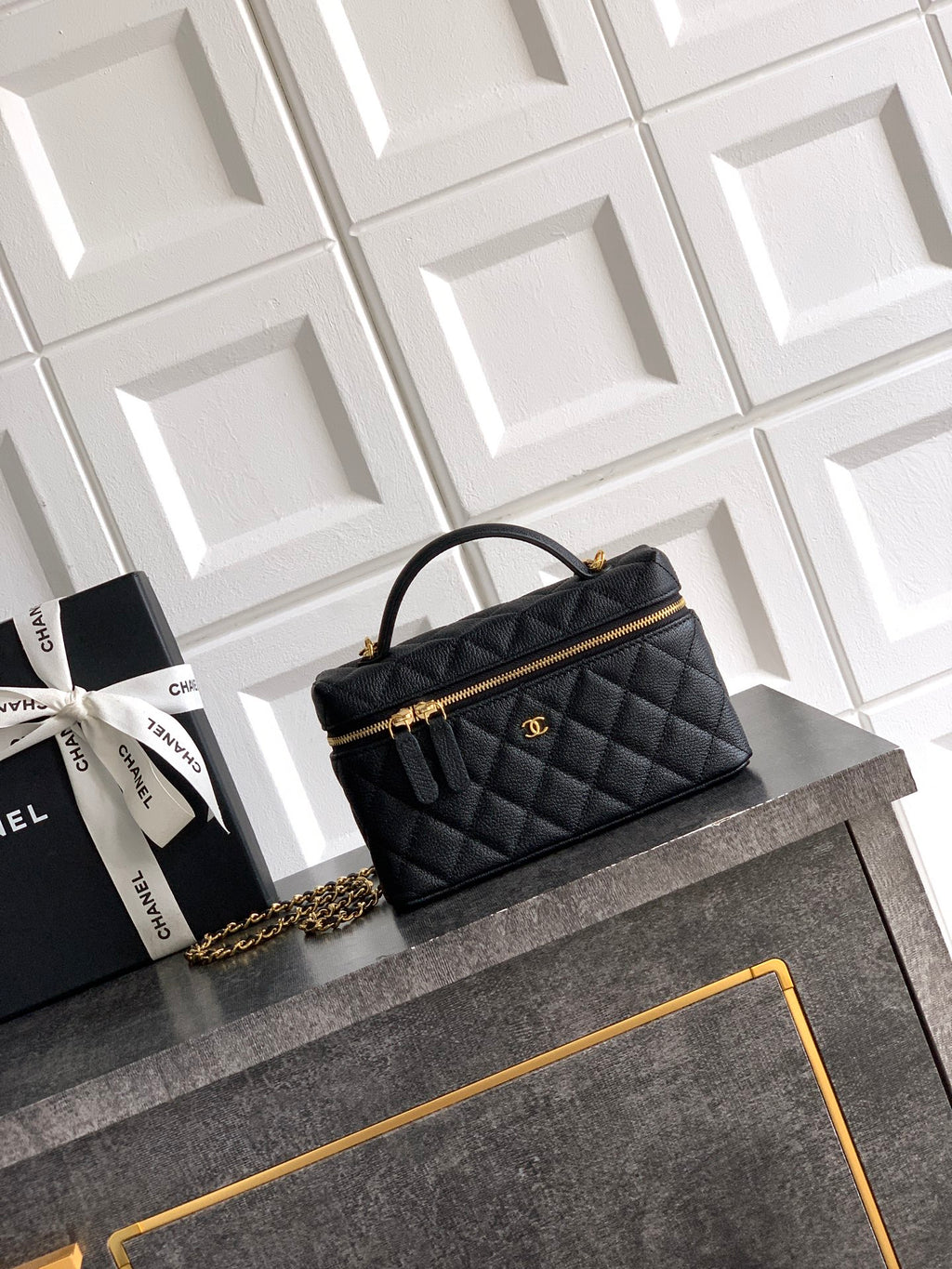 Black quilted handbag with gold chain strap and top handle, zip closure.