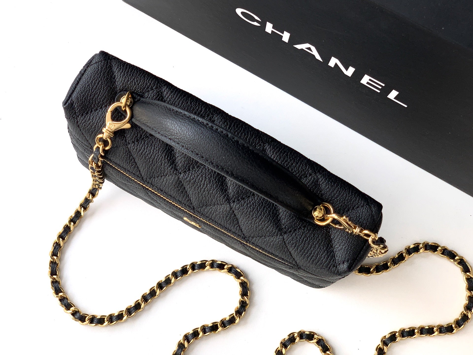 Black quilted crossbody bag with gold chain strap and gold zipper trim.