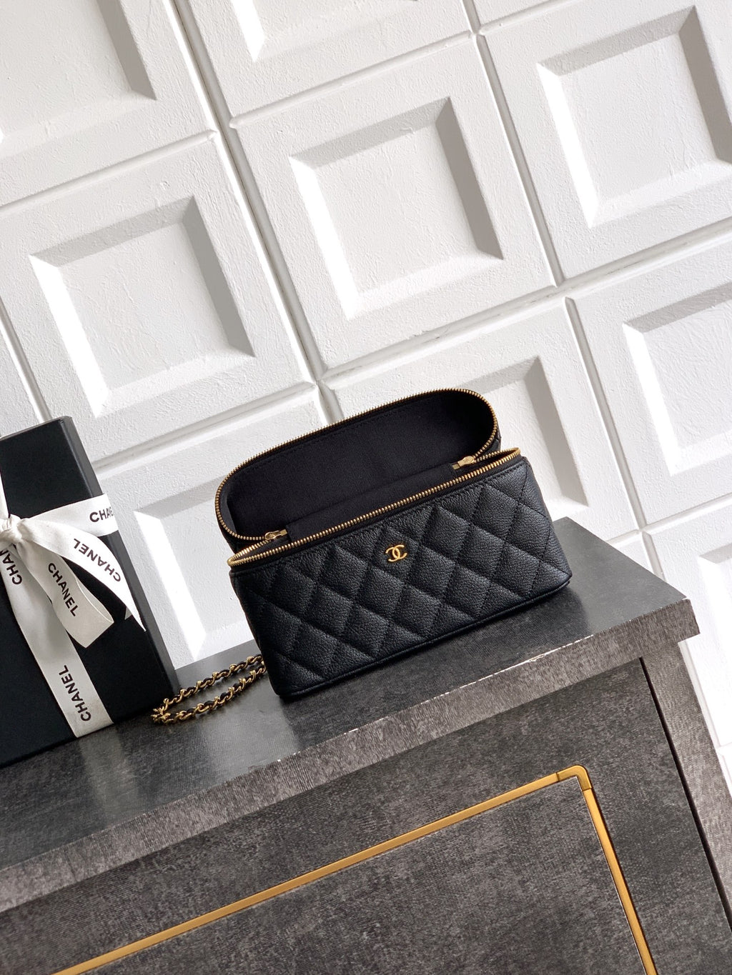 Black quilted handbag with gold chain strap and zip top, small logo plaque.