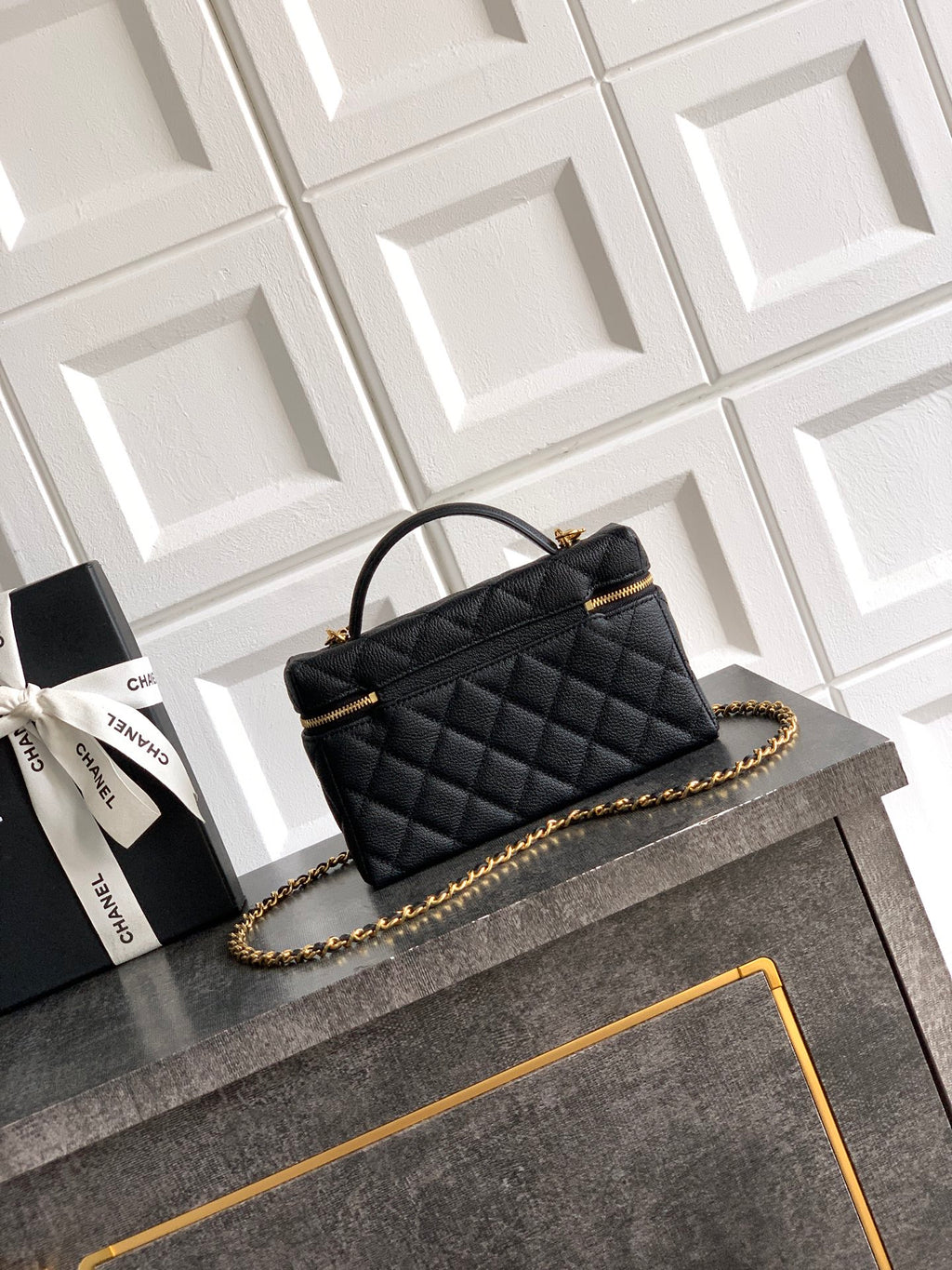 Black quilted handbag with gold chain shoulder strap and top handle, zip closure.