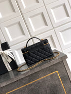 Black quilted handbag with gold chain shoulder strap and top handle, zip closure.
