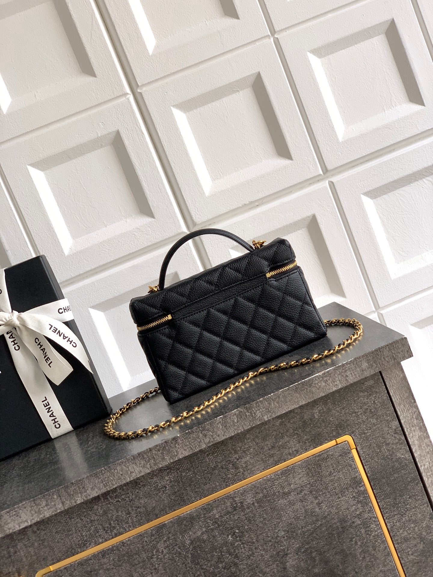 Black quilted handbag with gold chain shoulder strap and top handle, zip closure.