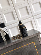 Black quilted mini handbag with gold chain strap and top handle, zip closure.