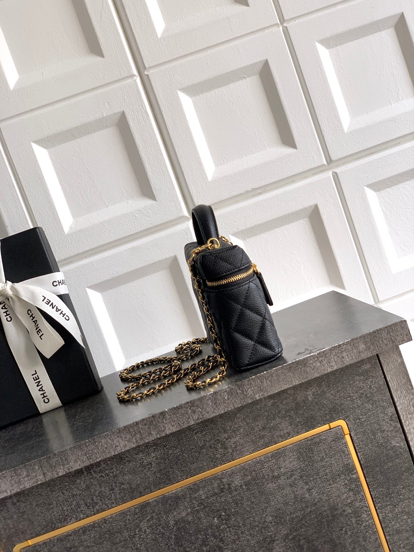 Black quilted mini handbag with gold chain strap and top handle, zip closure.