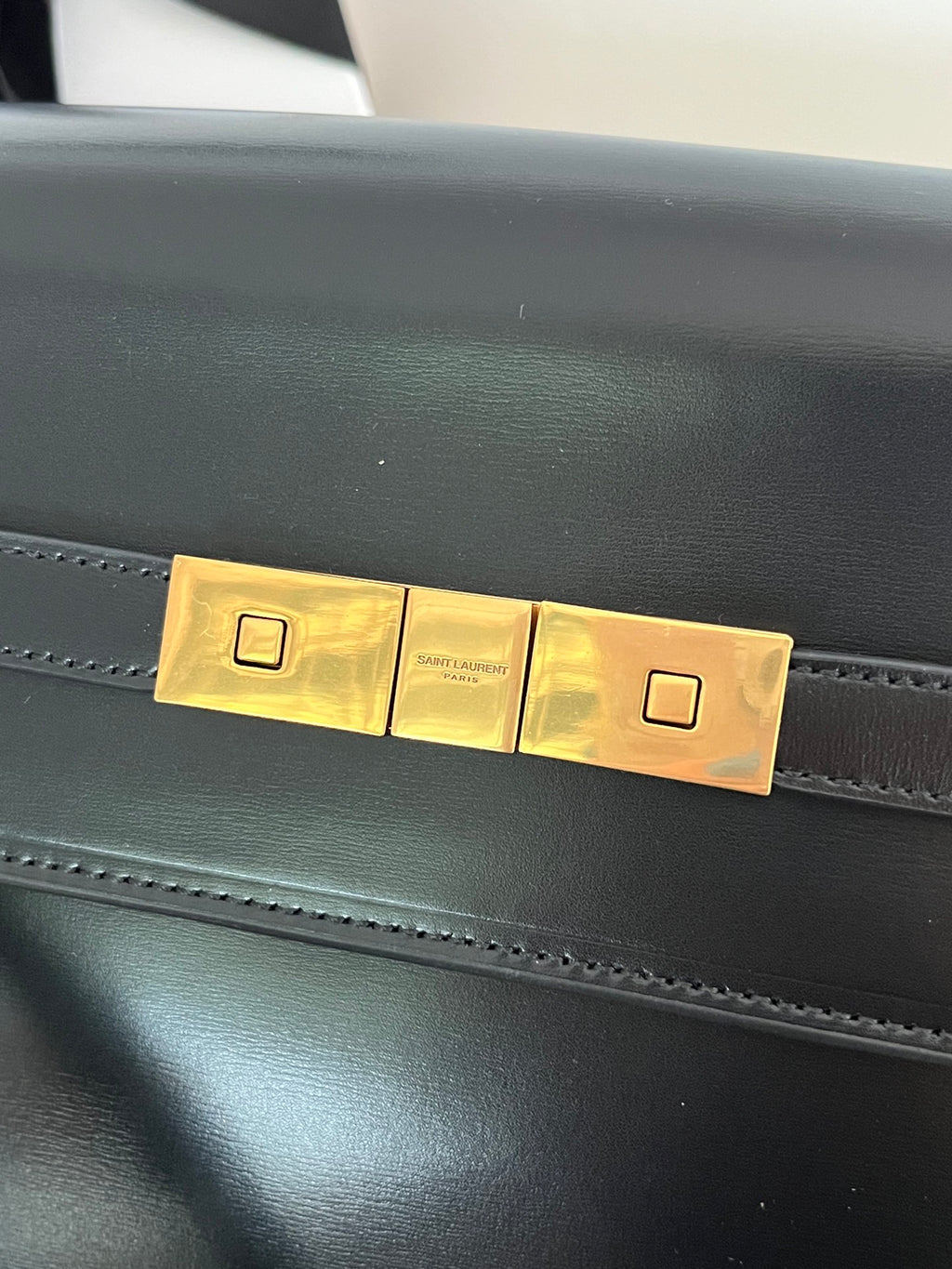 YSL bag clasp close-up with gold-tone plate and dark leather front panel