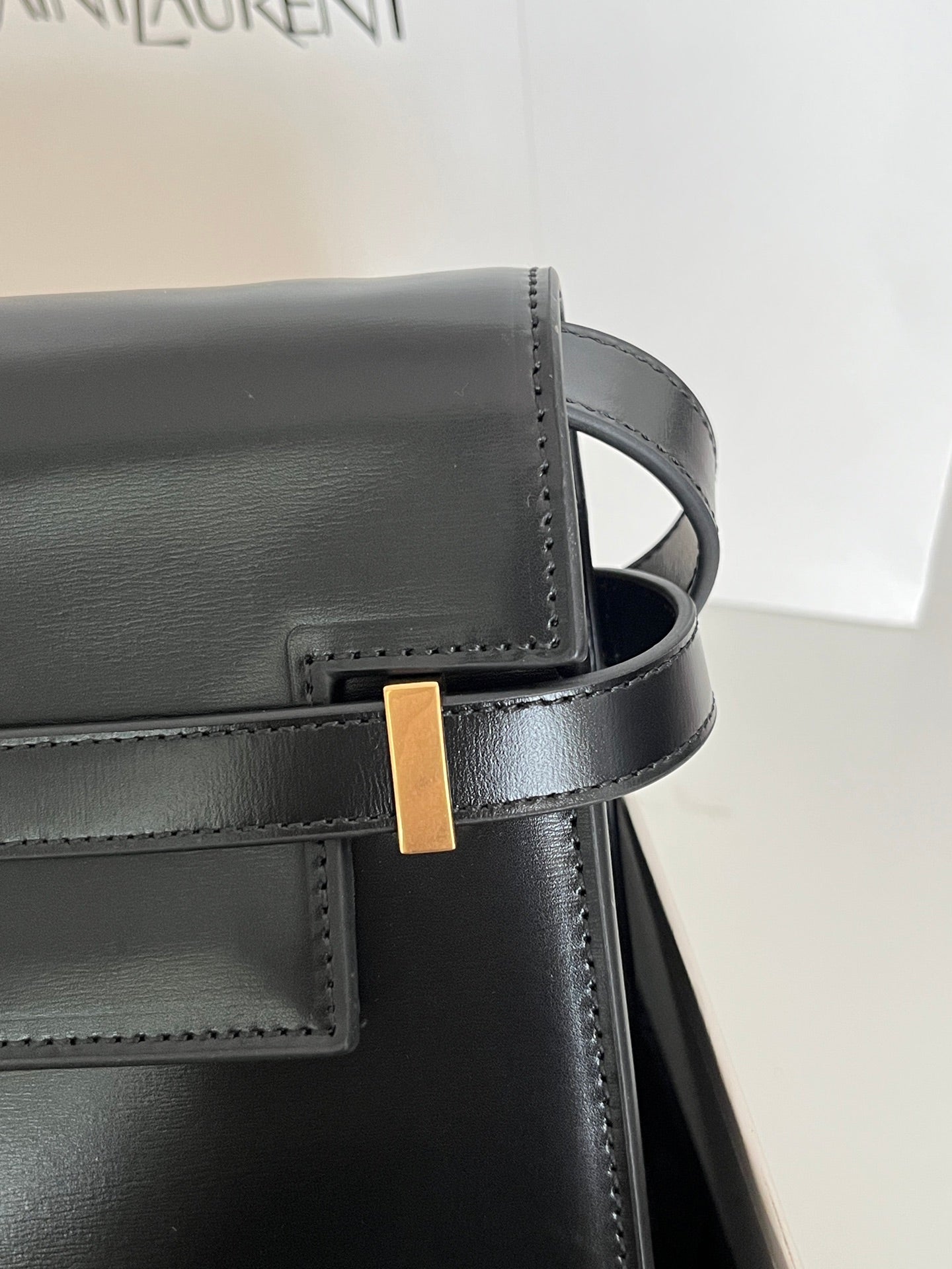YSL bag strap close-up with gold-tone buckle and dark leather stitching