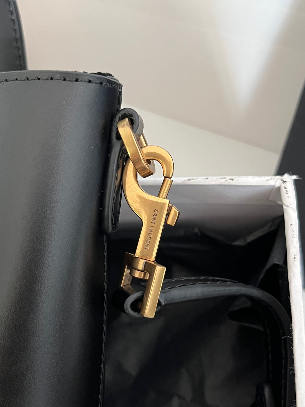Dark gray leather tote bag close-up of gold carabiner clasp and side hardware