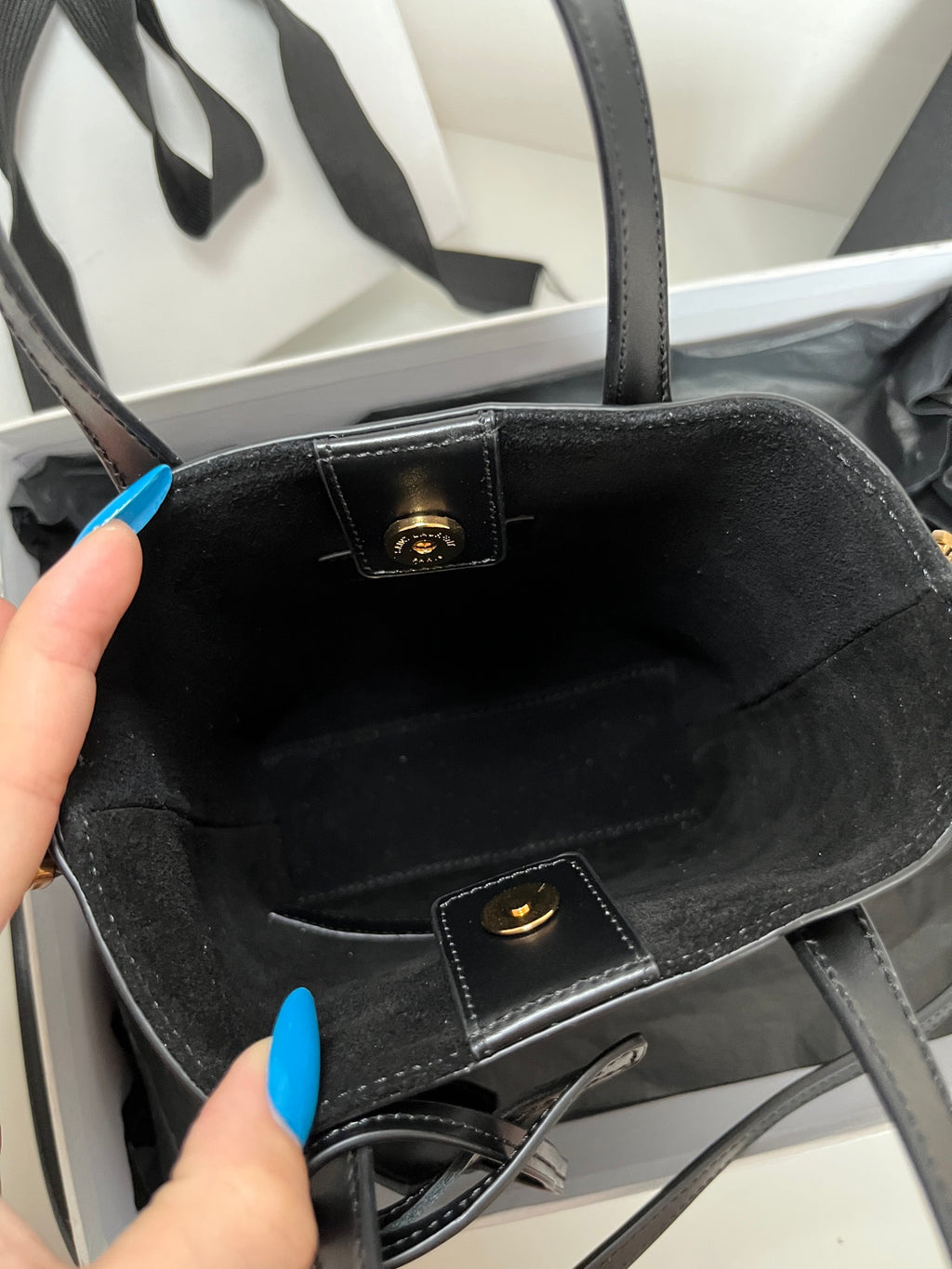 Dark tote bag interior view with logo plaque and inner pocket strap detail
