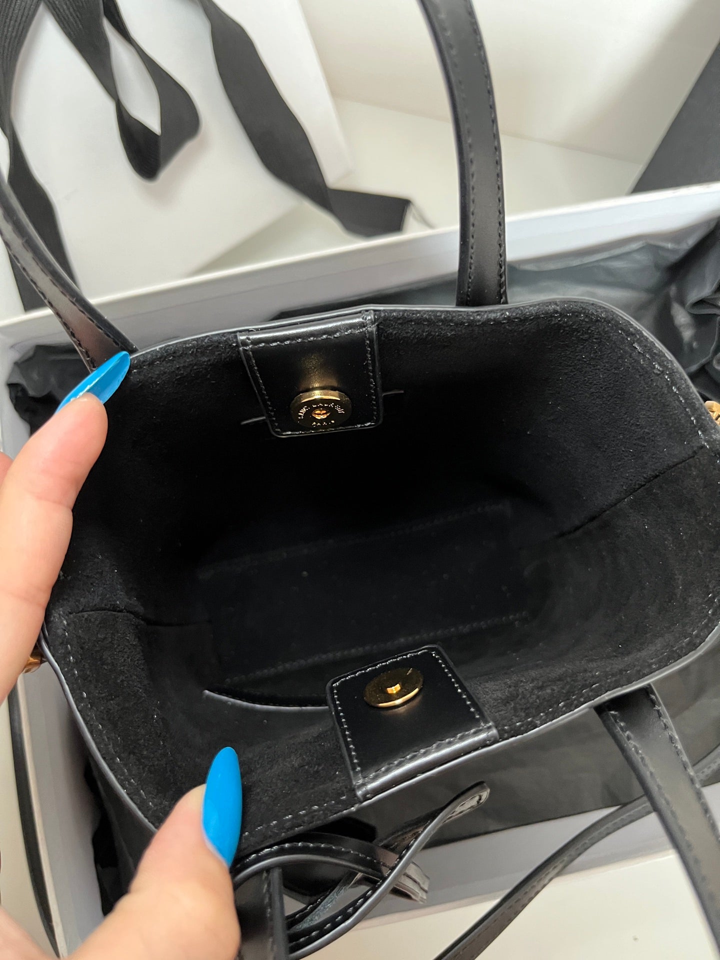 Dark tote bag interior view with logo plaque and inner pocket strap detail