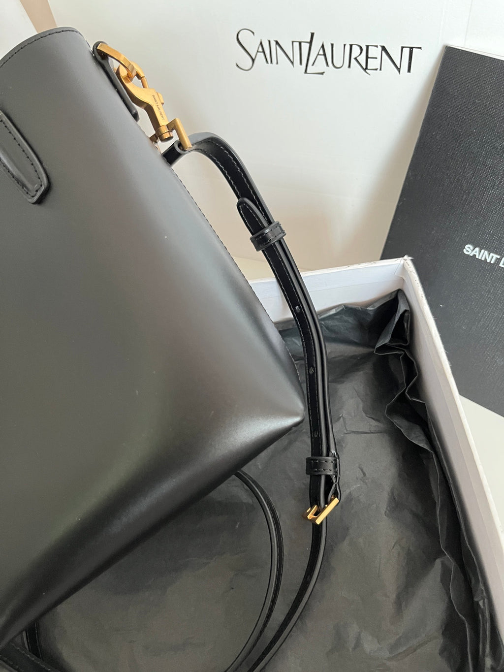 Dark gray leather tote bag showing side strap and gold clasp hardware