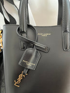 Dark gray leather tote bag front view with embossed logo patch and strap detail