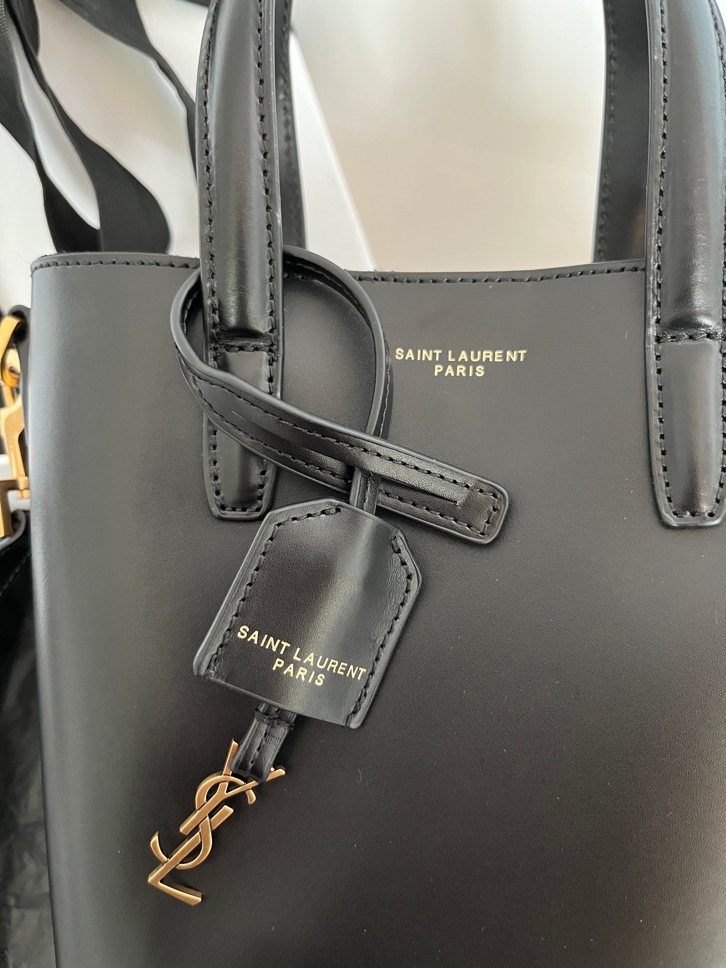 Dark gray leather tote bag front view with embossed logo patch and strap detail
