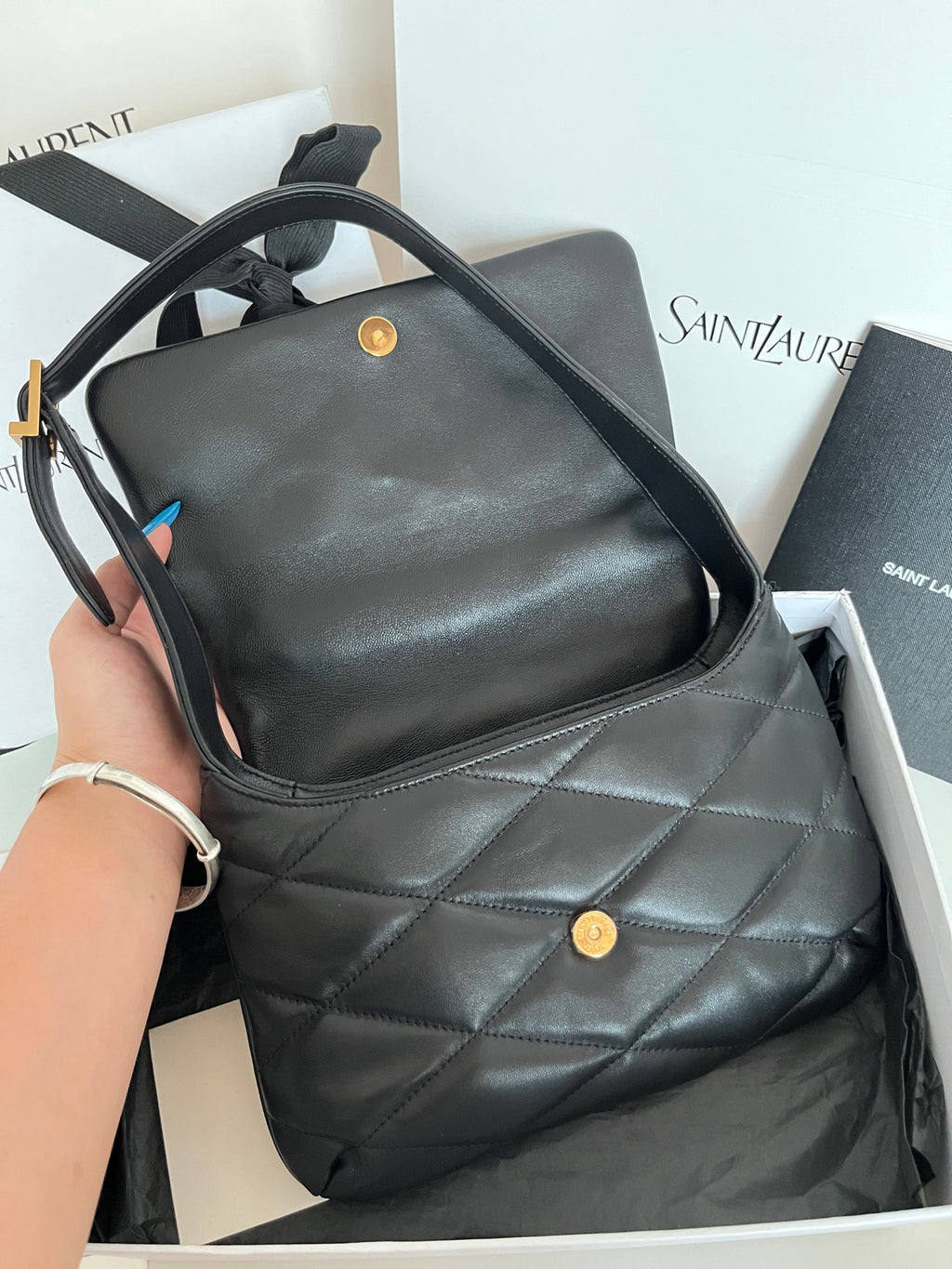 Quilted dark leather tote-style bag with top handles and gold logo button on front