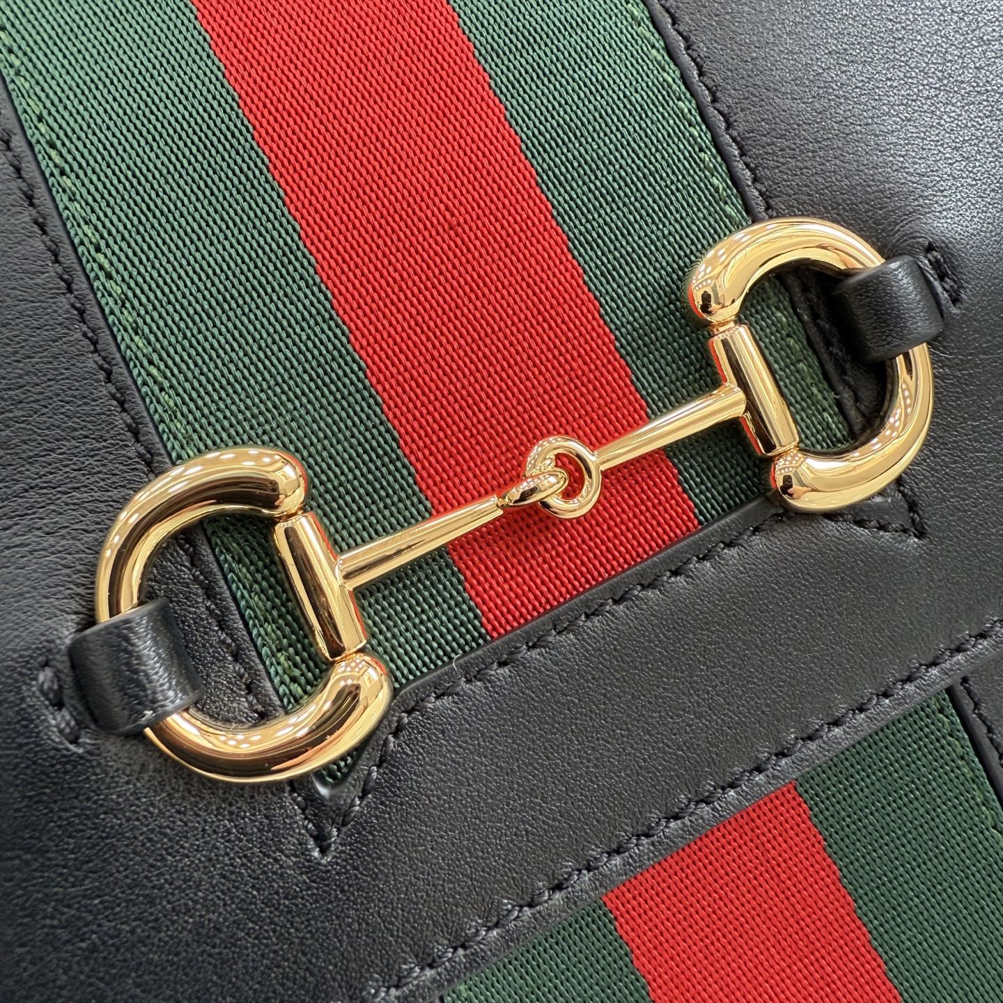 Gold-tone clasp detail on black leather Gucci strap with green and red stripe