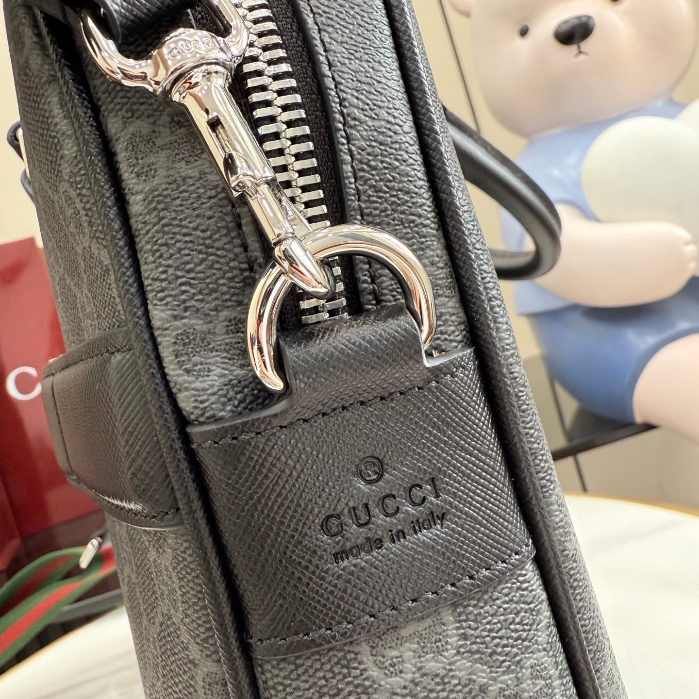 Gucci bag closeup: dark textured leather front, logo panel, metal zipper pull