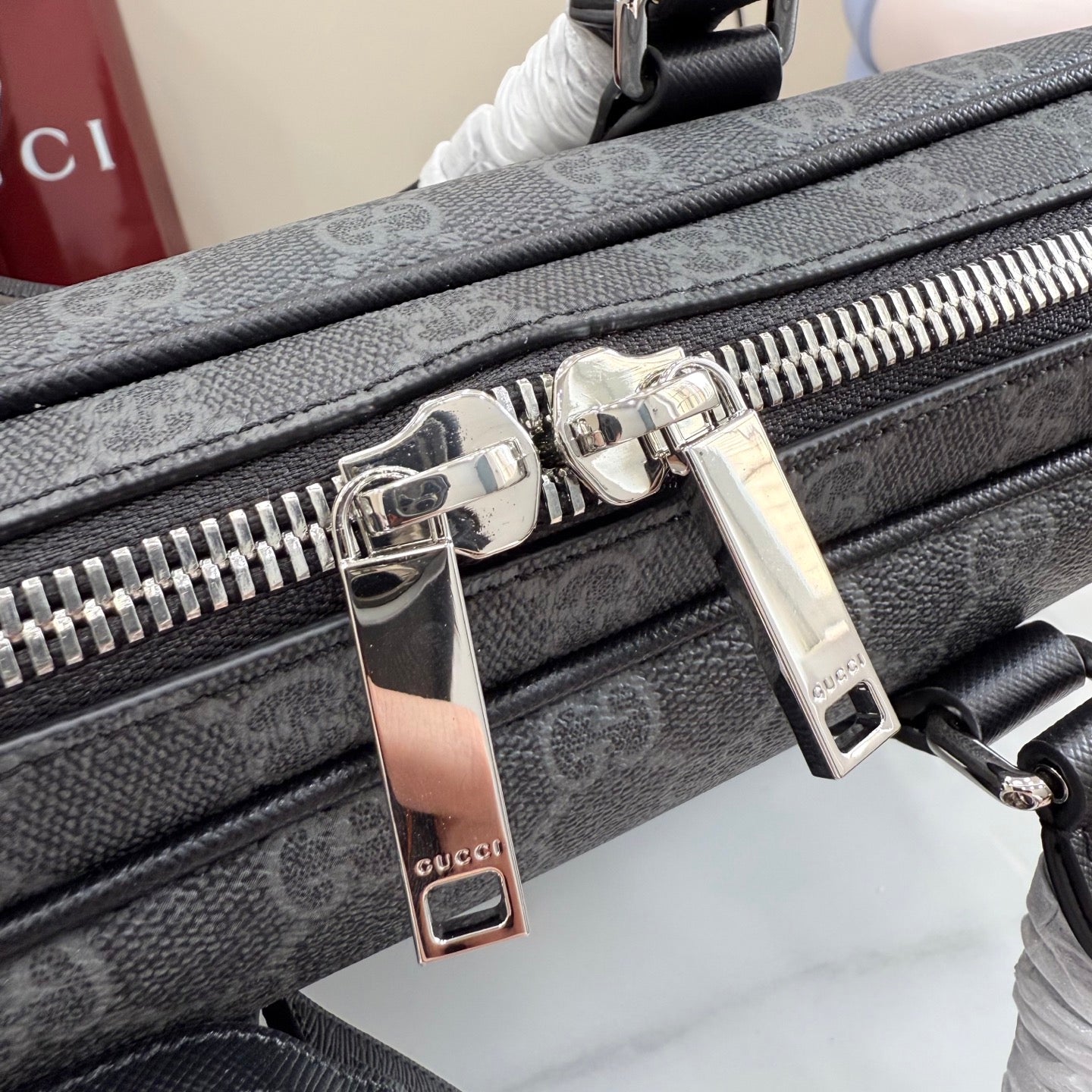 Front zipper pull hardware on GG monogram bag with metal tags and teeth track.