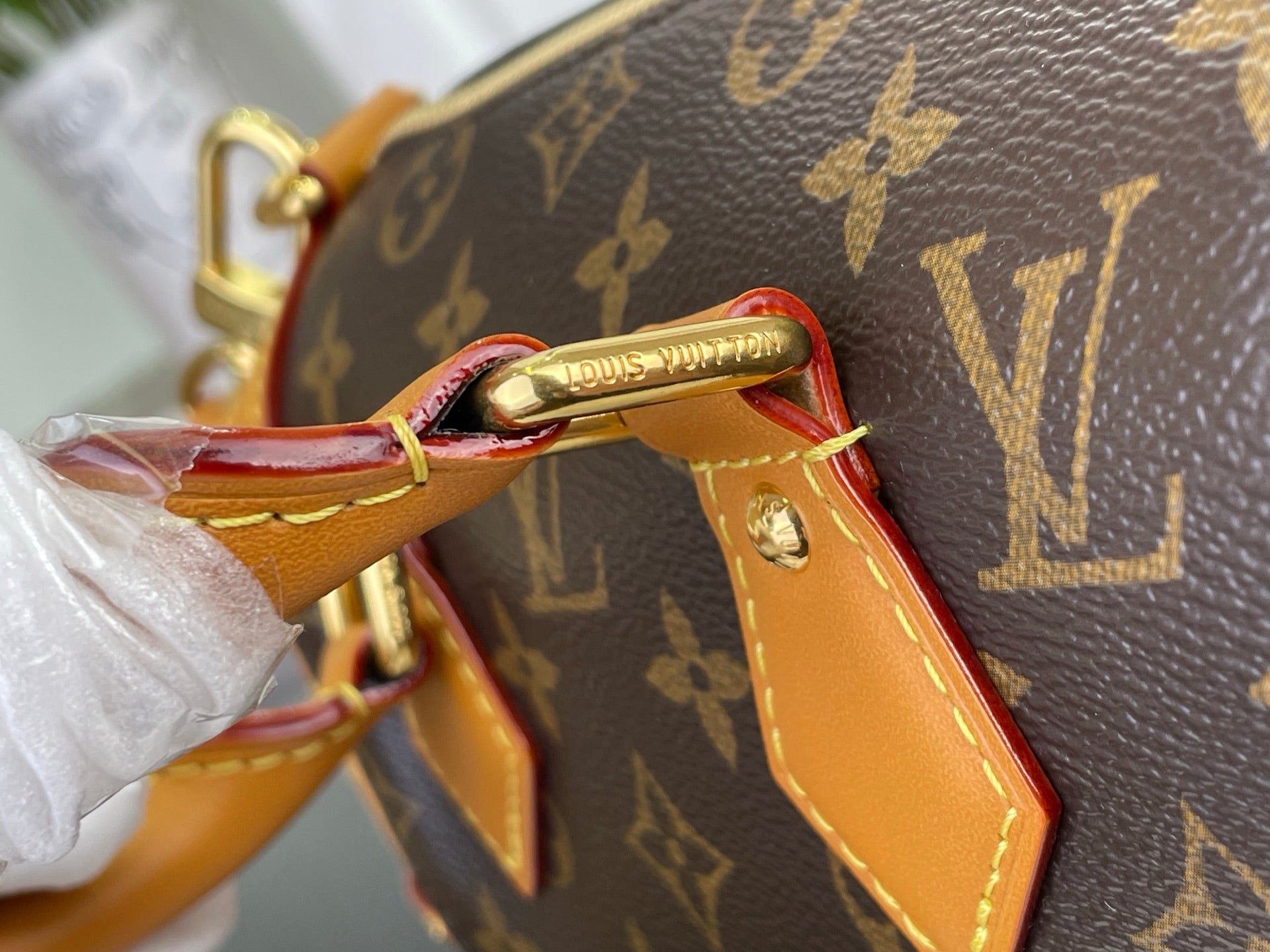 Gold clasp and tan leather trim on monogram handbag with stitched edges
