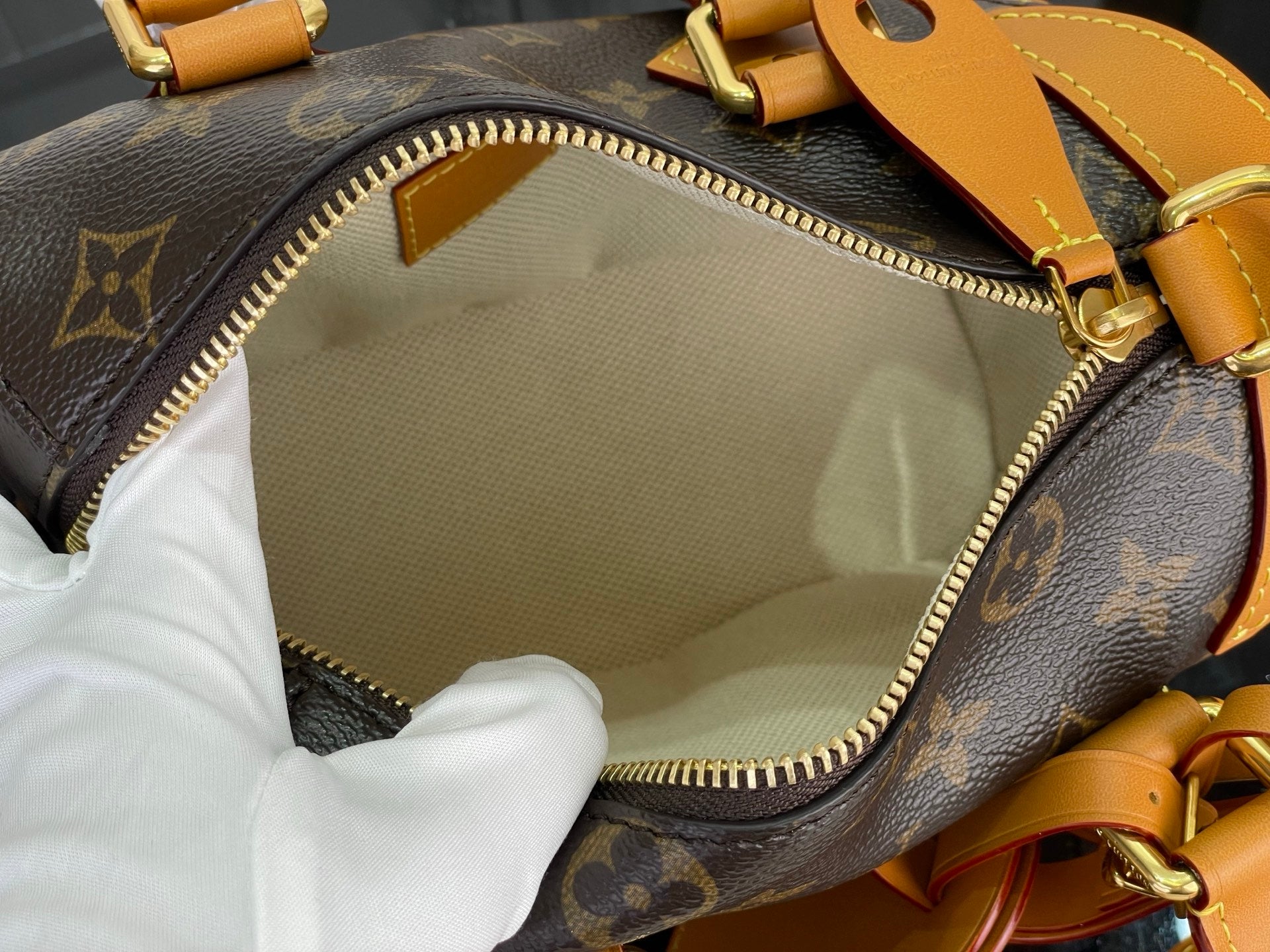 Zippered bag opening with beige lining and gold zipper on brown monogram exterior