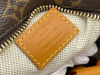 Tan leather inner label with embossed text and yellow edge stitching on monogram fabric