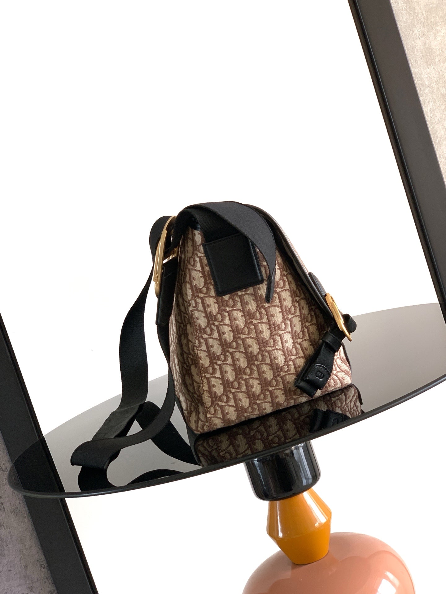 Dior bag front view with black strap and beige monogram canvas flap, gold buckle.