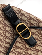 Dior bag strap detail with gold oval ring and black leather tab on monogram canvas.