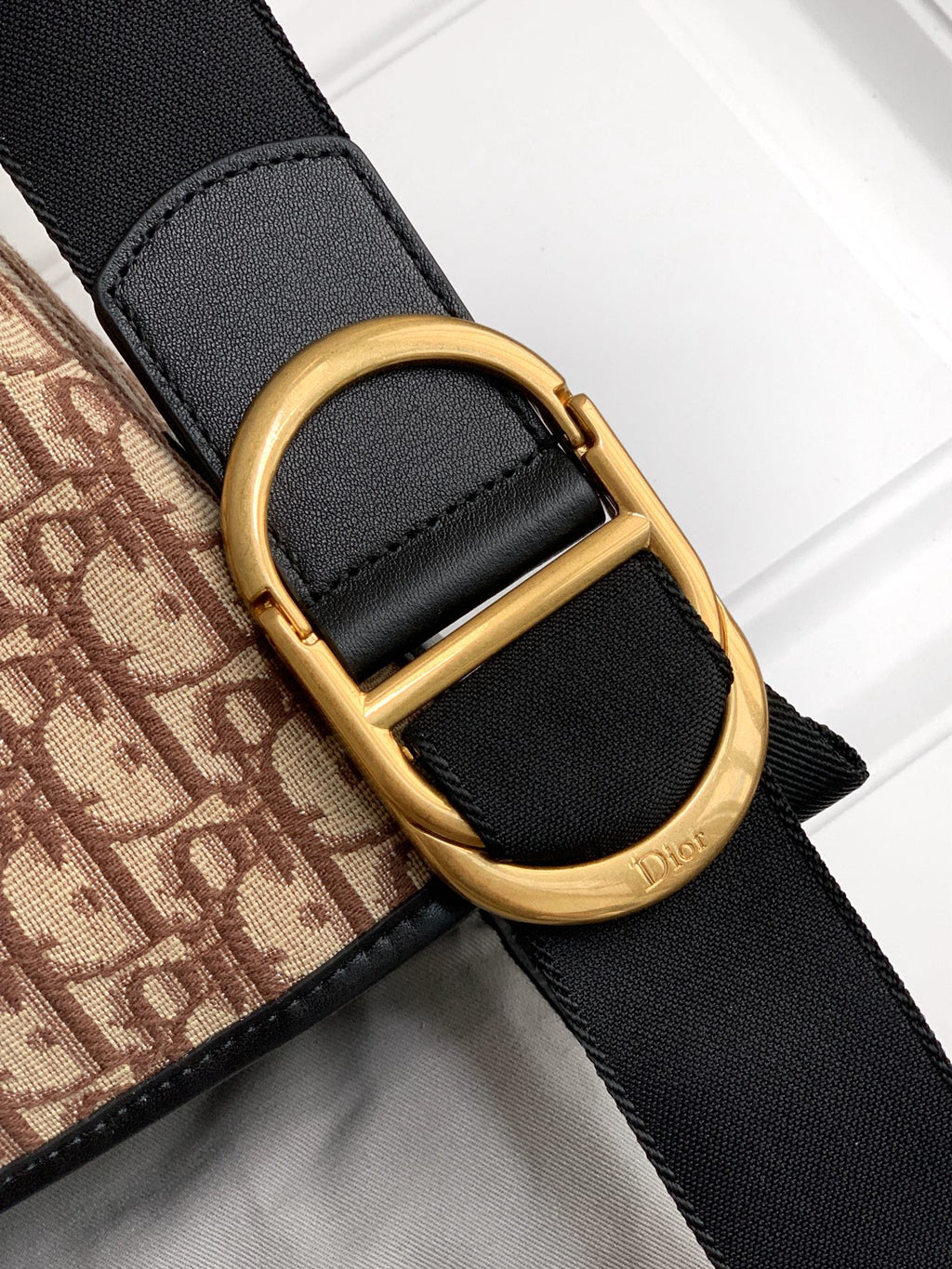 Dior bag strap detail with black fabric and gold buckle ring, Dior branding patch.